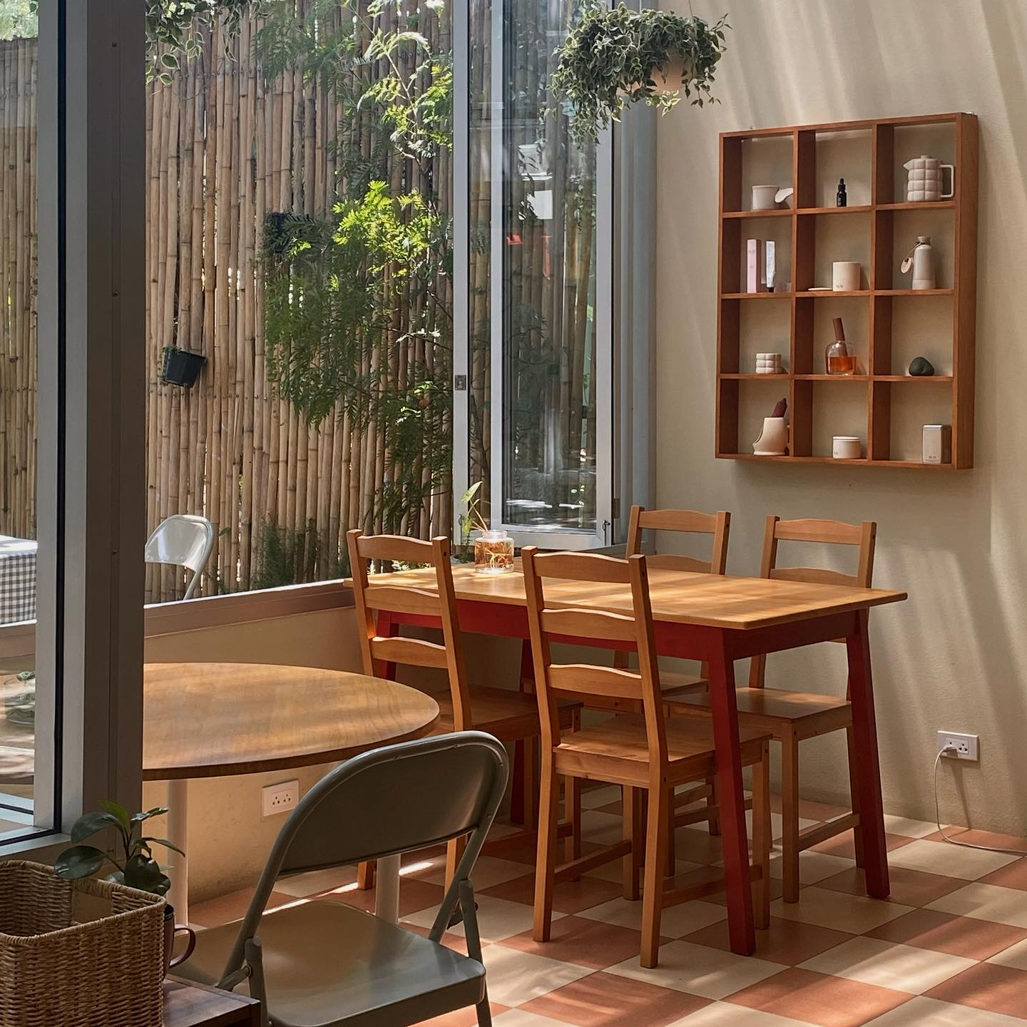 พื้นที่รับประทานอาหารที่สว่างไสวด้วยแสงแดด มีโต๊ะและเก้าอี้ไม้ โต๊ะกลมกับเก้าอี้โลหะ ชั้นวางของติดผนัง และหน้าต่างบานใหญ่ที่มองเห็นสวนไผ่—มุมสบายๆ ที่สะท้อนเสน่ห์ผ่อนคลายของการเที่ยวเชียงใหม่.