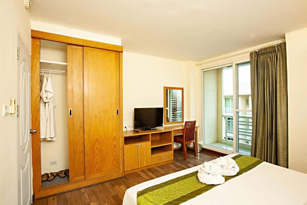 ห้องพักโรงแรมที่ ที่พักอยุธยา มีเตียงนอนที่แสนสบาย โต๊ะทำงาน เก้าอี้ โทรทัศน์ ตู้เสื้อผ้าไม้พร้อมผ้าคลุมอาบน้ำ และประตูที่เปิดออกไปยังระเบียงพร้อมผ้าม่าน—เหมาะสำหรับการเข้าพักของคุณในอยุธยา.