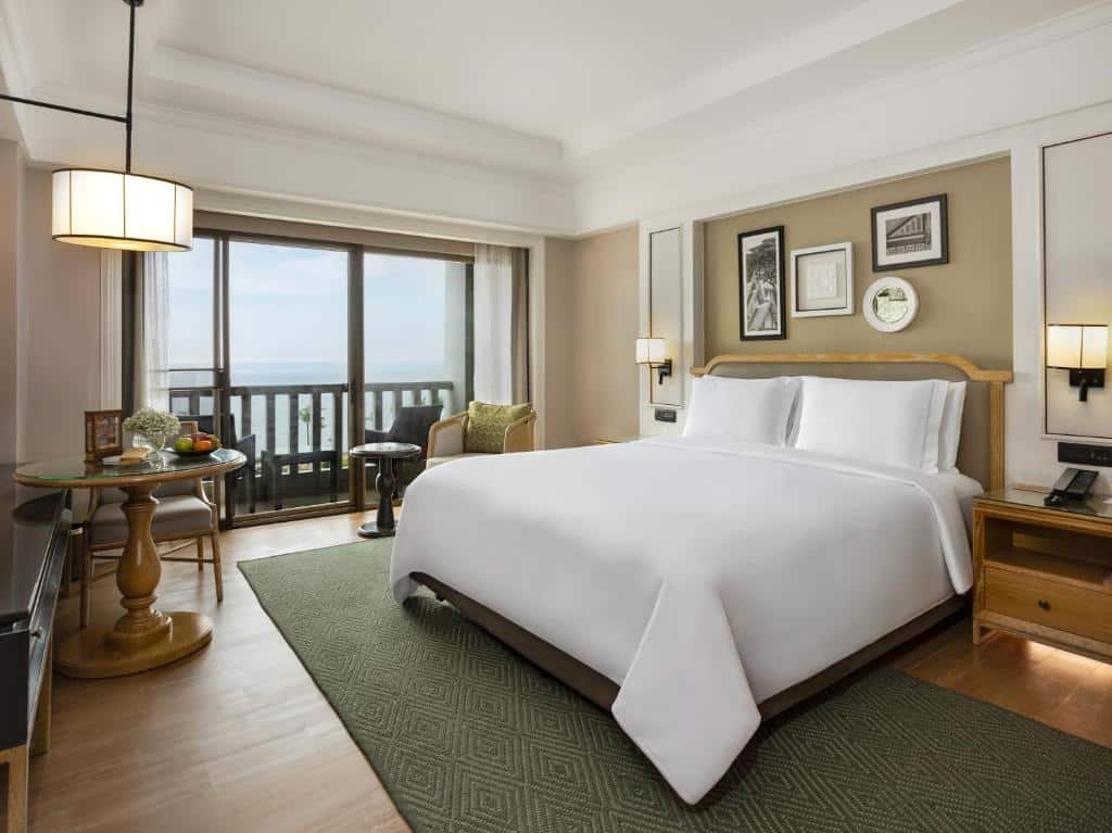 ห้องพักโรงแรมพร้อมเตียงคู่ที่จัดไว้อย่างเรียบร้อย เฟอร์นิเจอร์ไม้ โต๊ะกลมขนาดเล็กพร้อมเก้าอี้ งานศิลปะติดผนังในกรอบ และระเบียงพร้อมวิวภายนอก—เหมาะสำหรับผู้ที่มองหาที่พักหัวหินราคาประหยัดและบรรยากาศสบายๆ ใกล้ทะเล.