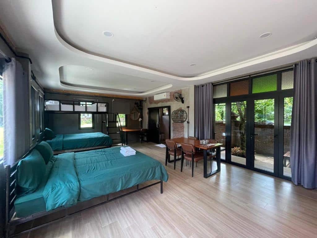 ห้องพักกว้างขวางพร้อมเตียงสองเตียงที่ปกคลุมด้วยผ้าสีเขียว โต๊ะรับประทานอาหารไม้ หน้าต่างบานใหญ่พร้อมผ้าม่านสีเทา และวิวทิวทัศน์สีเขียว—เหมาะสำหรับการเข้าพักที่ โรงแรมอยุธยา ที่มอบความสะดวกสบายและการผ่อนคลายในทุกมุม.