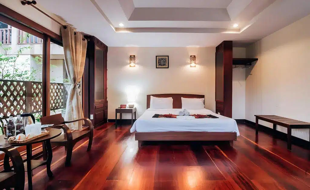 เตียงคู่ที่จัดไว้อย่างเรียบร้อยในห้องกว้างขวางพร้อมพื้นไม้ โต๊ะพร้อมเก้าอี้ ตู้เสื้อผ้าแบบเปิด และระเบียงพร้อมผ้าม่านที่ปล่อยให้แสงธรรมชาติส่องเข้ามา—เหมาะสำหรับการเข้าพักของคุณที่ ที่พักปัว.