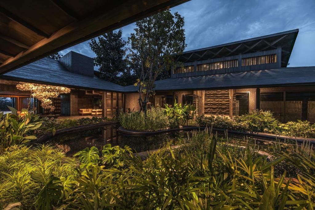 บ้านสมัยใหม่พร้อมหน้าต่างบานใหญ่ล้อมรอบลานสวนเขียวชอุ่มและสระน้ำกลางบ้าน ส่องสว่างด้วยแสงไฟอบอุ่นยามพลบค่ำ—เหมาะสำหรับผู้ที่มองหาที่พักในตัวเมืองน่านหรือที่พักสไตล์ทันสมัยในบรรยากาศเงียบสงบ.