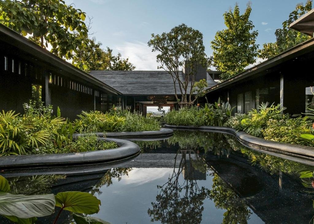 อาคารสมัยใหม่ใน ที่พักน่านในเมือง มีลานกลางที่เต็มไปด้วยต้นไม้เขียวชอุ่มและน้ำพุสะท้อนแสงล้อมรอบด้วยทางเดินโค้ง.