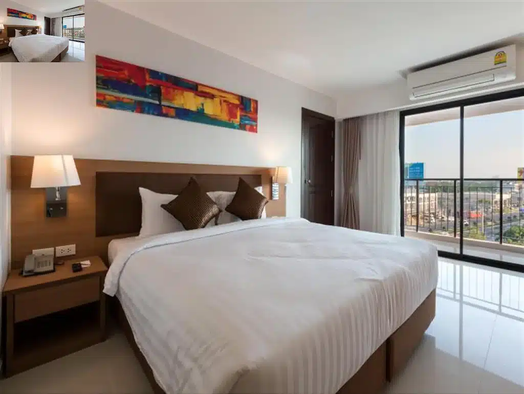 ห้องพักหัวหินสไตล์โมเดิร์นพร้อมเตียงขนาดใหญ่ โต๊ะข้างเตียงสองตัวพร้อมโคมไฟ ภาพศิลปะนามธรรมสีสันสดใสเหนือหัวเตียง และหน้าต่างที่มองเห็นวิวเมืองอันสวยงาม.