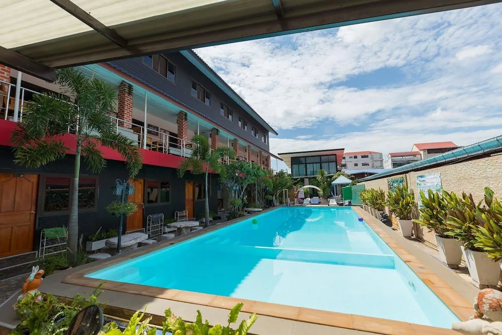 สระว่ายน้ำกลางแจ้งที่มีน้ำสีฟ้าใสสะอาด ล้อมรอบด้วยเก้าอี้อาบแดดและอาคารหลายชั้นภายใต้ท้องฟ้าที่มีเมฆบางส่วน—เหมาะสำหรับการพักผ่อนที่ โรงแรมอยุธยา.