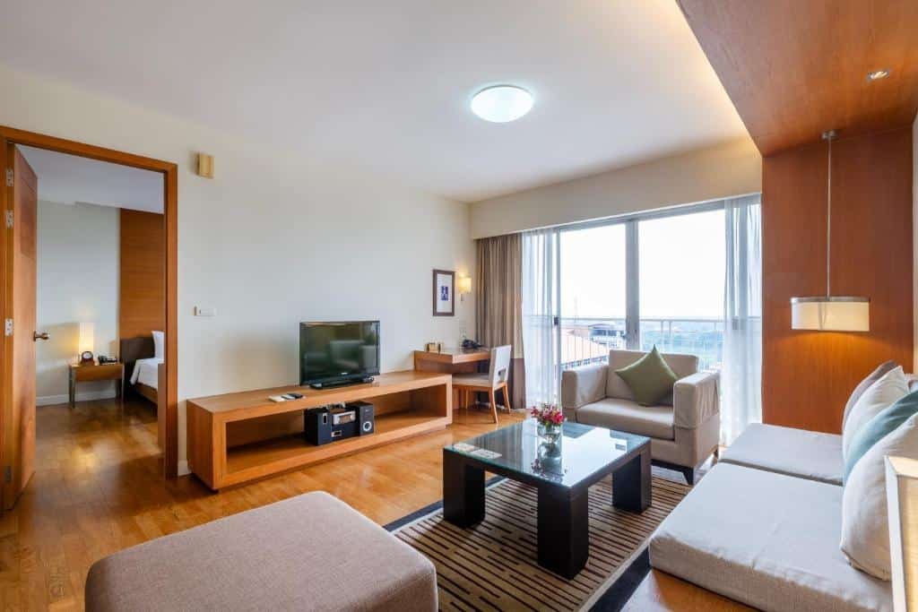 ห้องนั่งเล่นสไตล์โมเดิร์นพร้อมพื้นไม้ โซฟาสีเรียบ โต๊ะกาแฟกระจก และแสงธรรมชาติ—เหมาะสำหรับการพักผ่อนหลังจากสำรวจที่พักอยุธยา หรือเพลิดเพลินกับความสะดวกสบายของโรงแรมอยุธยา.