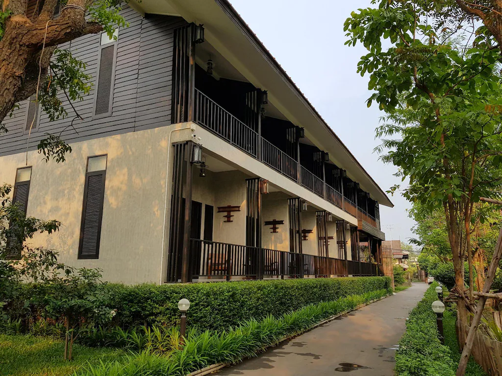 อาคารสองชั้นสไตล์โมเดิร์นพร้อมระเบียงร่มรื่น ล้อมรอบด้วยพื้นที่สีเขียวและทางเดินปูพื้น เหมาะอย่างยิ่งสำหรับผู้ที่มองหาที่พักในอยุธยาในบรรยากาศเงียบสงบและทันสมัย.