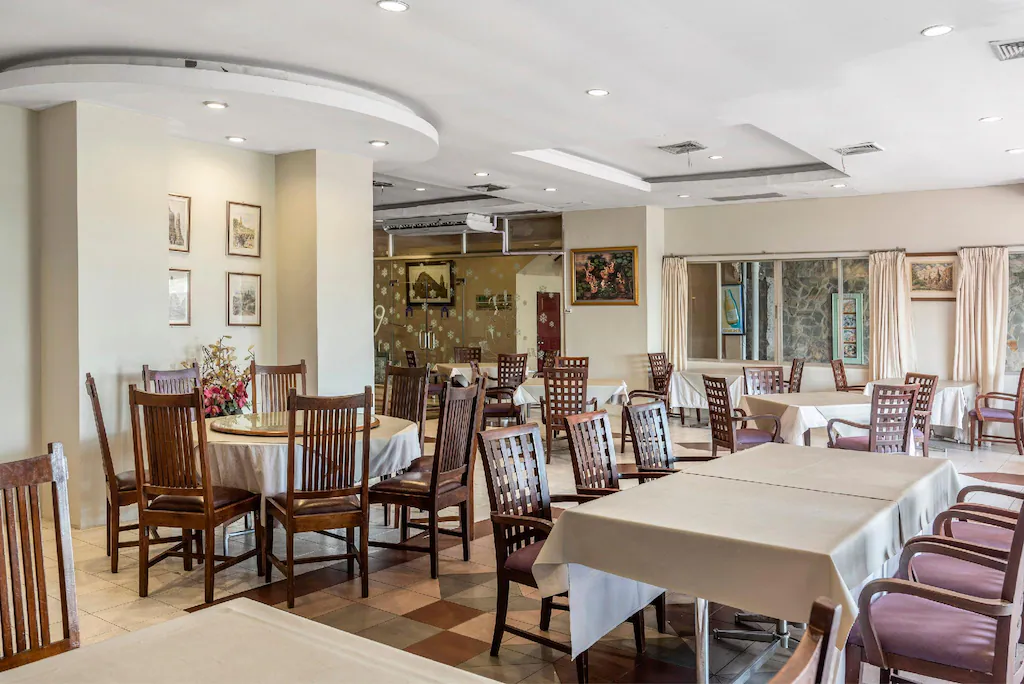 พื้นที่รับประทานอาหารพร้อมโต๊ะและเก้าอี้ไม้หลายตัว ผ้าปูโต๊ะสีขาว ภาพศิลปะในกรอบแขวนบนผนัง และหน้าต่างบานใหญ่พร้อมผ้าม่านสีเบจ—เหมาะสำหรับการพักผ่อนหลังจากวันแห่งการสำรวจสถานที่ท่องเที่ยวในอยุธยา.