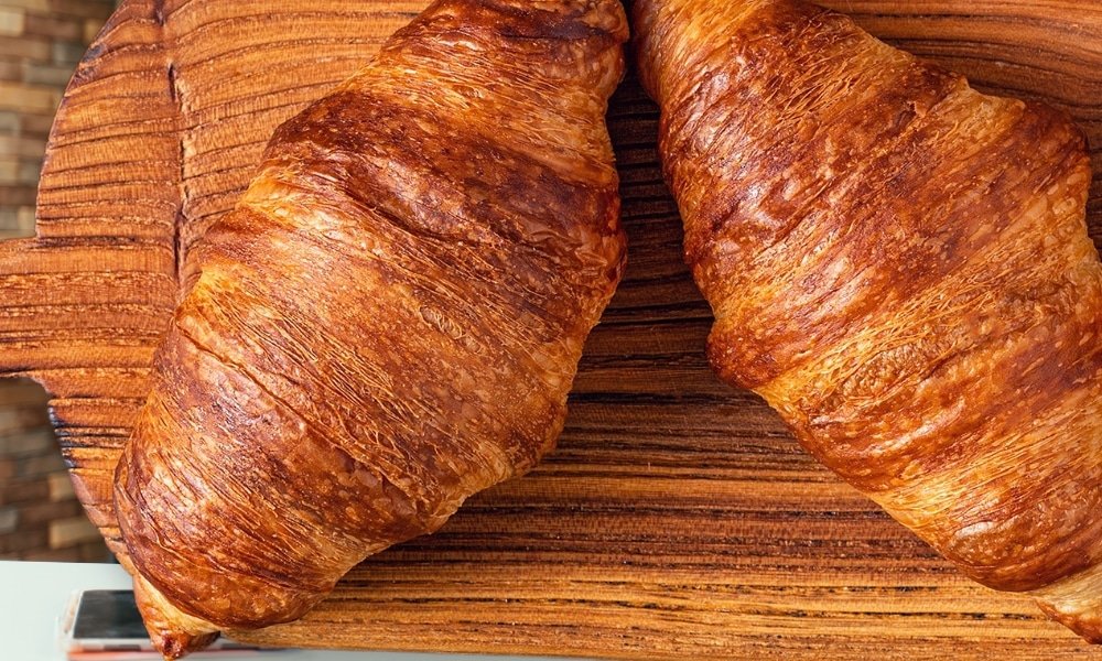 ครัวซองต์สีน้ำตาลทองสองชิ้นวางอยู่บนเขียงไม้—เหมาะสำหรับมื้อเช้าก่อนที่คุณจะออกไปสำรวจสถานที่ท่องเที่ยวในเชียงใหม่และค้นพบคาเฟ่สุดน่ารักใจกลางเมืองเชียงใหม่.