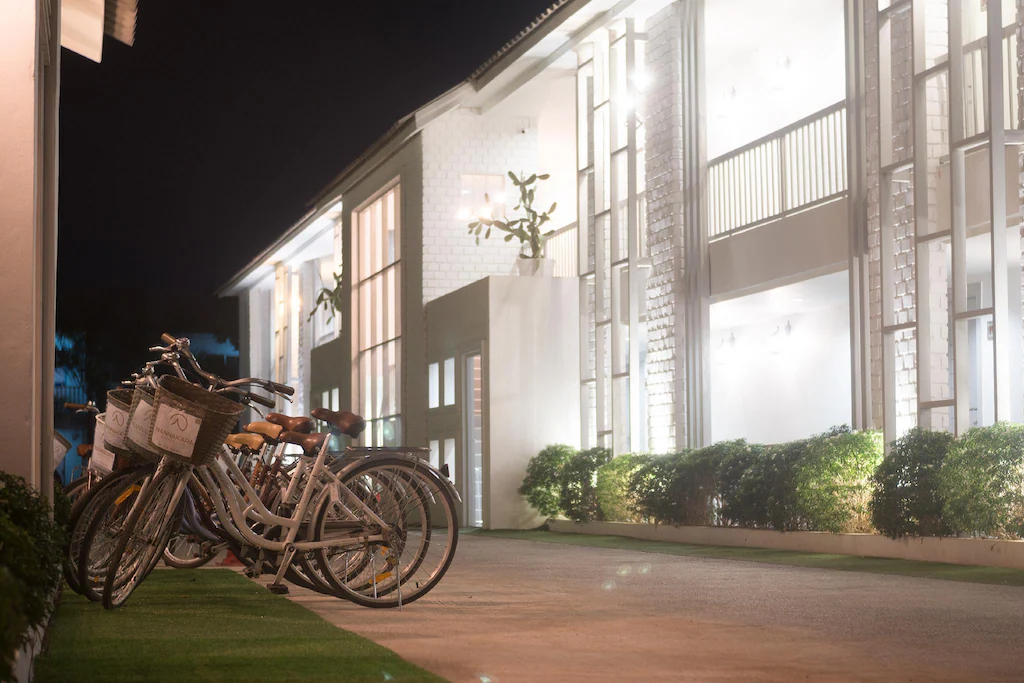 มีจักรยานหลายคันจอดอยู่บนทางเดินปูพื้นนอกอาคารสีขาวที่ทันสมัยและสว่างไสวในยามค่ำคืน สร้างบรรยากาศที่อบอุ่นต้อนรับสำหรับผู้มาเยือนที่กำลังมองหาที่พักในน่านหรือที่พักสะดวกสบายในบริเวณนี้.