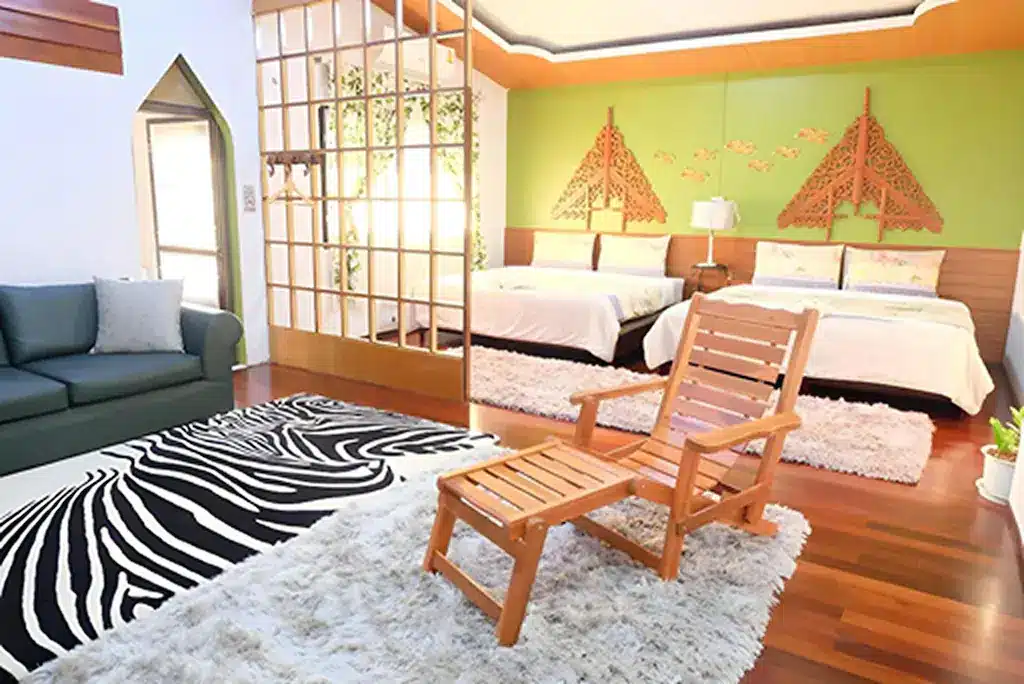 ห้องนอนสมัยใหม่ที่ ที่พักอยุธยาริมน้ำ พร้อมเตียงสองเตียง ผนังสีเขียวเป็นจุดเด่น พรมลายม้าลาย เก้าอี้ไม้และที่วางเท้า โซฟา และกระจกบานใหญ่สะท้อนพื้นที่ที่มีสไตล์.