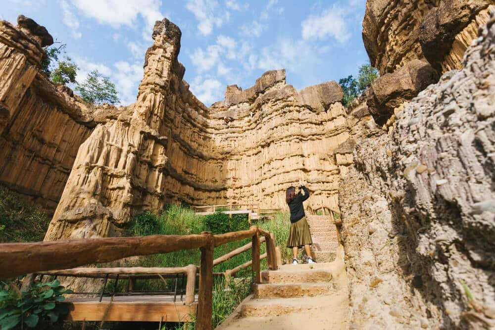 บุคคลที่ยืนอยู่บนบันไดหินซึ่งล้อมรอบด้วยหินชั้นสูงใหญ่ใต้ท้องฟ้าที่มีเมฆบางส่วน—การผจญภัยรออยู่ที่สถานที่ท่องเที่ยวเชียงใหม่.