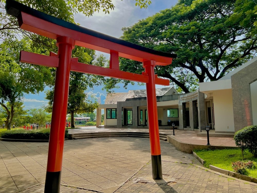 ประตูโทริอิสีแดงตั้งตระหง่านอยู่ที่ทางเข้าลานบ้าน ล้อมรอบด้วยอาคารสมัยใหม่และต้นไม้ใหญ่—เป็นจุดที่น่าดึงดูดสำหรับผู้ที่ต้องการค้นพบสถานที่ลับในระหว่างการเดินทางท่องเที่ยวอยุธยา.