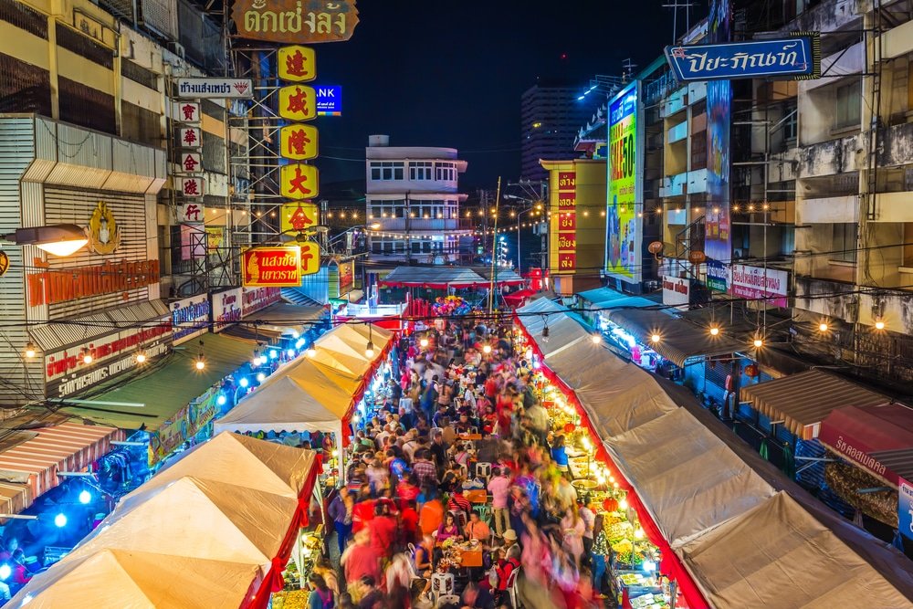 ตลาดกลางคืนที่คึกคักเต็มไปด้วยแผงขายของมากมาย แสงไฟสีสันสดใส และป้ายไฟนีออนในบรรยากาศเมืองยามค่ำคืน—เป็นหนึ่งในสถานที่ท่องเที่ยวเชียงใหม่ที่ต้องไปเยือนสำหรับผู้ที่ต้องการสัมผัสชีวิตยามค่ำคืนที่คึกคัก.