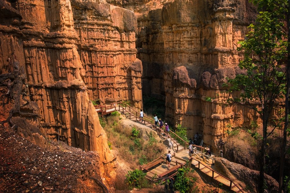 กลุ่มคนเดินไปตามทางเดินไม้ที่ล้อมรอบด้วยหินทรายสูงใหญ่และขรุขระในหุบเขา—อัญมณีที่ซ่อนอยู่สำหรับผู้ที่ต้องการสำรวจ ที่เที่ยวเชียงใหม่.