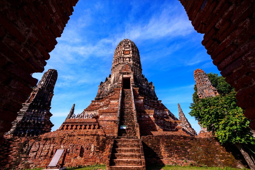 วัดโบราณก่ออิฐ มียอดแหลมตรงกลางและบันไดชัน ล้อมรอบด้วยซุ้มประตูโค้งอิฐสีแดง ท่ามกลางท้องฟ้าสีฟ้าสดใส—สถานที่ท่องเที่ยวอยุธยาที่ต้องไปเยือน สำหรับผู้ที่รักประวัติศาสตร์ที่มาเยือนสถานที่ท่องเที่ยวอยุธยา.