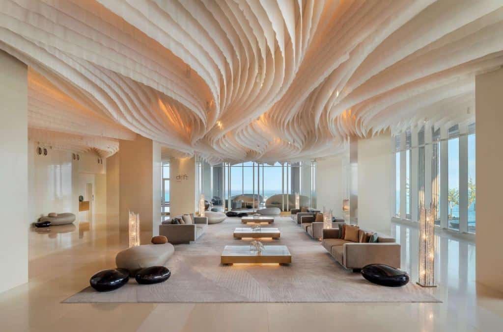 ห้องนั่งเล่นกว้างขวางทันสมัยพร้อมเพดานที่ออกแบบอย่างประณีต โซฟาโทนสีกลาง โต๊ะเตี้ย โคมไฟตั้งพื้น และหน้าต่างบานใหญ่ที่มองเห็นวิวทะเลที่ โรงแรมพัทยาติดทะเล สำหรับการพักผ่อนริมชายหาดที่สมบูรณ์แบบ.