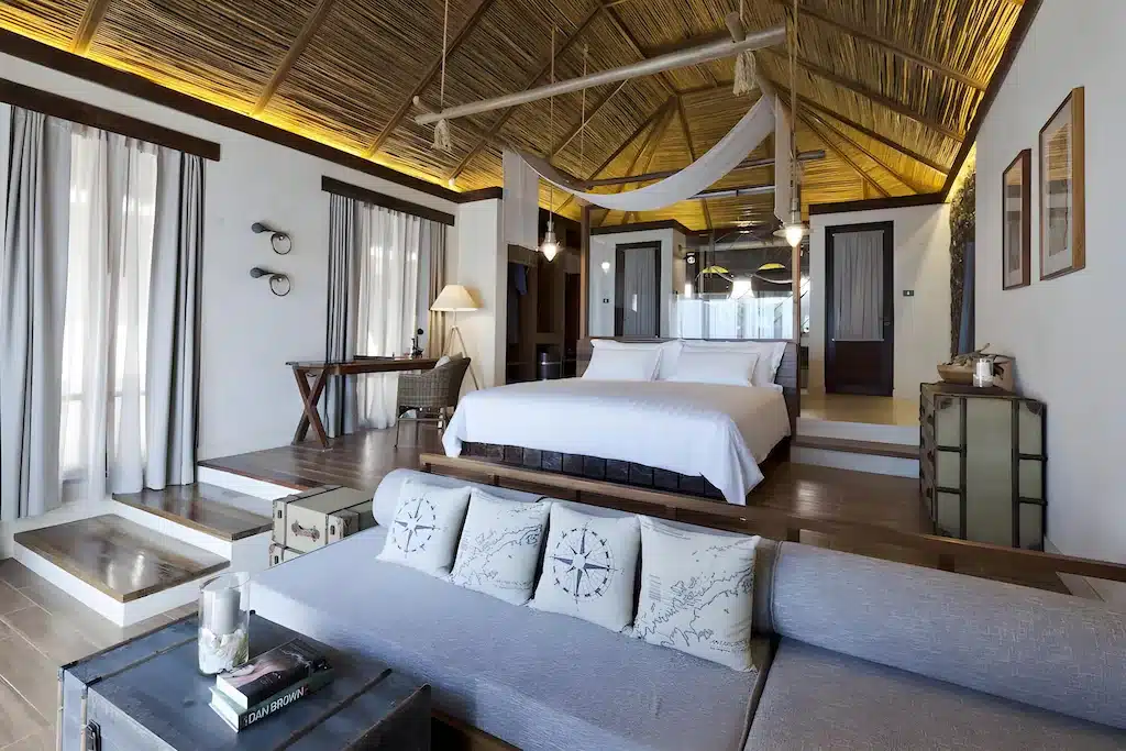 ห้องนอนกว้างขวางที่ โรงแรมพัทยาติดทะเล พร้อมเตียงขนาดใหญ่ โซฟา โต๊ะทำงาน และการตกแต่งแบบชนบทที่มีเพดานลาดและไม้ธรรมชาติ—เหมาะสำหรับการพักผ่อนริมชายหาดอย่างแท้จริง.