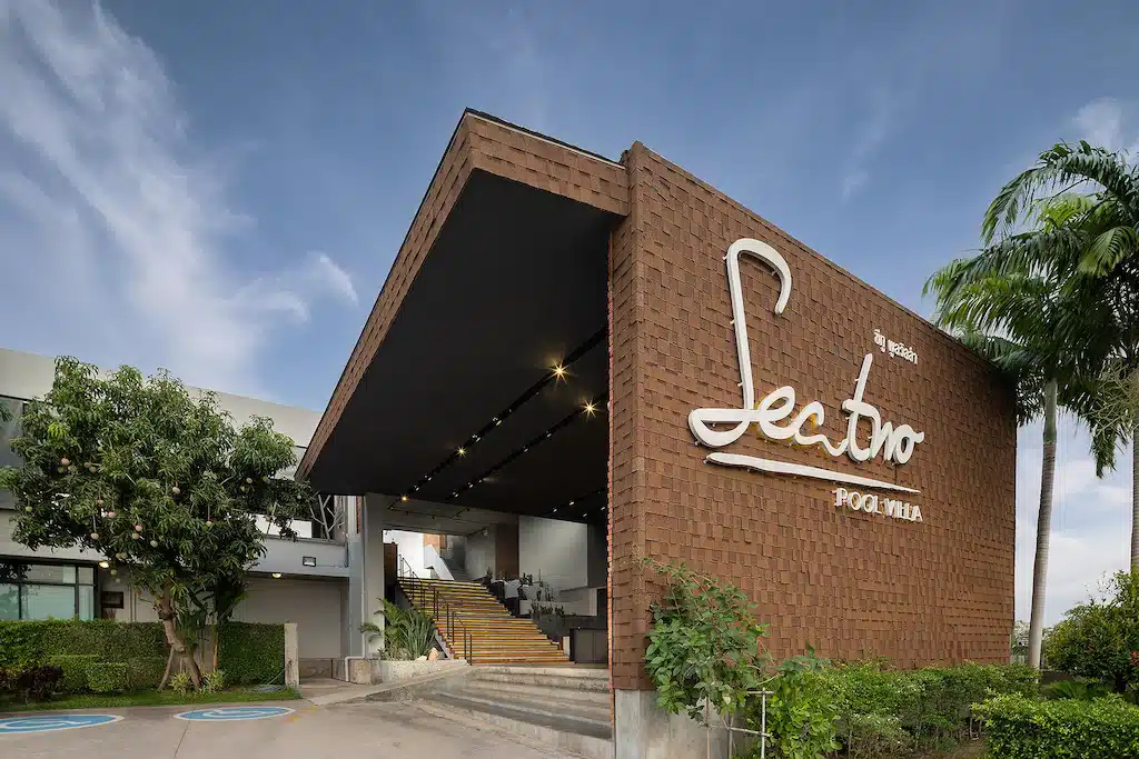 อาคารสมัยใหม่ที่มีหลังคาขนาดใหญ่และมุมเหลี่ยม พร้อมป้าย "Sector" บนด้านหน้า โรงแรมติดทะเลพัทยา รายล้อมไปด้วยต้นไม้สีเขียวและต้นปาล์มภายใต้ท้องฟ้าสีคราม.