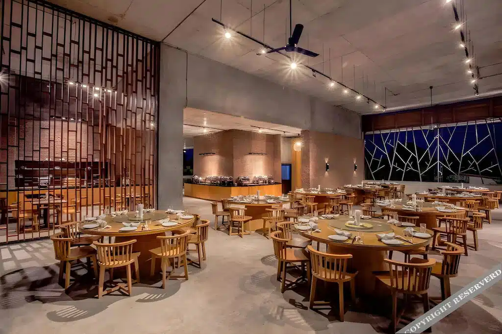 ร้านอาหารสมัยใหม่ภายในตกแต่งด้วยโต๊ะกลมและเก้าอี้ไม้สำหรับรับประทานอาหาร ผนังอิฐ พื้นที่บุฟเฟ่ต์ และพัดลมเพดานภายใต้แสงไฟสไตล์อุตสาหกรรม สร้างบรรยากาศหรูหราที่ โรงแรมติดทะเลพัทยา.