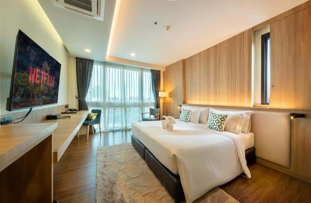 ห้องพักโรงแรมสมัยใหม่ที่ โรงแรมติดทะเลพัทยา พร้อมเตียงขนาดใหญ่  ที่พักระยอง ผนังไม้ ติดผนังทีวีพร้อม Netflix โต๊ะทำงาน เก้าอี้ และหน้าต่างบานใหญ่จากพื้นจรดเพดาน เพลิดเพลินกับวิวทะเลและผ้าขนหนูสะอาดพับไว้บนเตียงเพื่อความสะดวกสบายของคุณ.