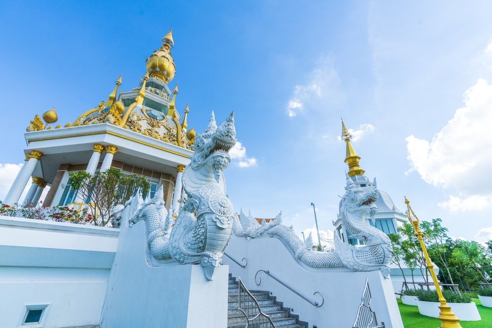 รูปปั้นมังกรขาวตั้งอยู่สองข้างบันไดที่นำไปสู่พระอุโบสถทองคำใต้ท้องฟ้าสีครามสดใส—สถานที่ท่องเที่ยวที่ไม่ควรพลาดในขอนแก่นสำหรับผู้ที่ต้องการสำรวจความมหัศจรรย์ของการท่องเที่ยวในขอนแก่น.