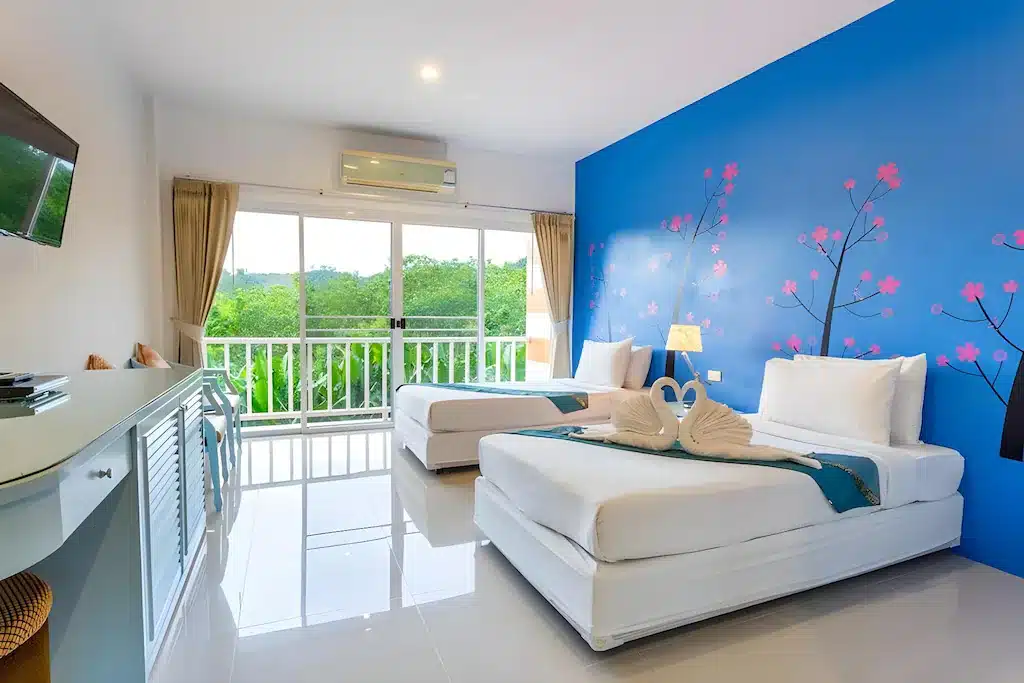 ห้องพักโรงแรมที่สว่างสดใส พร้อมด้วยเตียงเดี่ยวสองเตียง ผนังสีน้ำเงินที่ตกแต่งด้วยลวดลายดอกซากุระ ผ้าเช็ดตัวรูปหงส์ที่ดูสง่างาม ระเบียง และหน้าต่างขนาดใหญ่ที่เปิดรับวิวความเขียวขจีของธรรมชาติ—เหมาะอย่างยิ่งสำหรับผู้ที่กำลังมองหาที่พักเขาค้อ หรือประสบการณ์รีสอร์ทเขาค้อที่เต็มไปด้วยเสน่ห์.