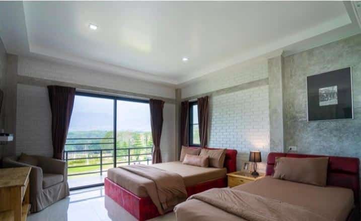 ห้องนอนสไตล์โมเดิร์นที่มีเตียงสองเตียง ชุดเครื่องนอนสีน้ำตาล โต๊ะทำงาน โต๊ะข้างเตียง โคมไฟ หน้าต่างขนาดใหญ่พร้อมม่านสีเข้ม และวิวพื้นที่สีเขียวด้านนอก — เหมาะอย่างยิ่งสำหรับผู้ที่มองหาที่พักเขาค้อ ที่ผสมผสานความสบายกับความงามของธรรมชาติ.
