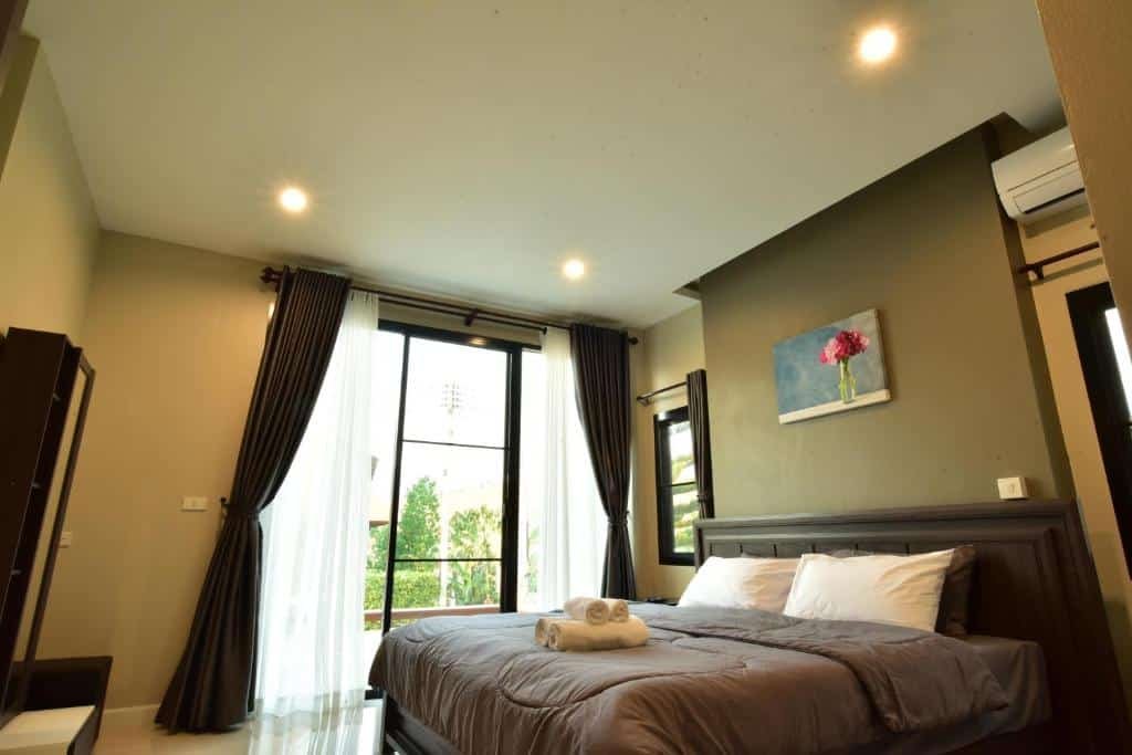 ห้องนอนสไตล์ทันสมัยที่รีสอร์ทเขาค้อ มีเตียงขนาดใหญ่พร้อมหัวเตียงสีเข้ม ผ้าเช็ดตัวที่พับไว้อย่างเรียบร้อย หน้าต่างสูงจากพื้นถึงเพดานพร้อมผ้าม่านที่ดูสง่างาม และภาพวาดดอกไม้สีแดงที่สะดุดตาแขวนอยู่เหนือเตียง.