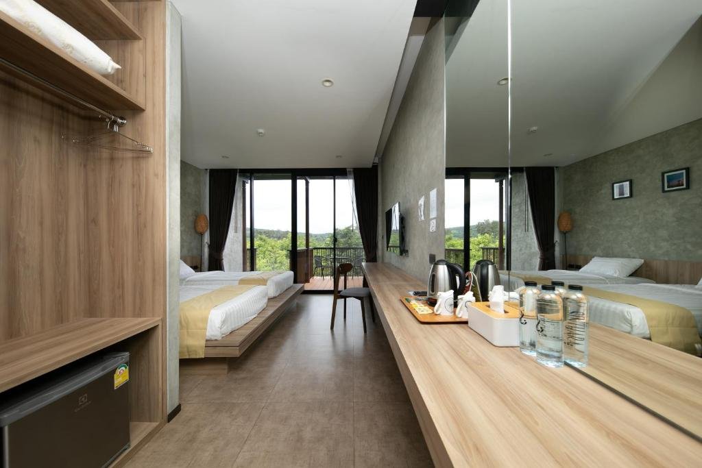 ห้องพักโรงแรมสมัยใหม่ที่มีเตียงสอง เที่ยวเชียงคาน  เตียง กระจกขนาดใหญ่ โต๊ะทำงาน มินิบาร์ น้ำดื่มบรรจุขวด และวิวต้นไม้ด้านนอกผ่านหน้าต่างสูงจากพื้นถึงเพดาน — เป็นจุดพักที่เหมาะที่สุดสำหรับการสำรวจสถานที่ท่องเที่ยวในขอนแก่นและสถานที่ท่องเที่ยวชั้นนำของขอนแก่น.