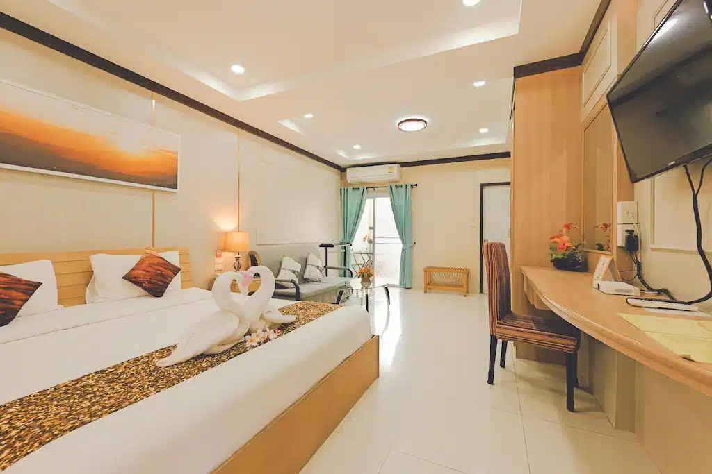ห้องพักโรงแรมที่จัดแต่งอย่างเรียบร้อย พร้อมด้วยเตียงขนาดใหญ่ ผ้าเช็ดตัวรูปหงส์ ทีวีจอแบน โต๊ะทำงาน โต๊ะเล็กพร้อมเก้าอี้ ประตูระเบียง และแสงไฟนุ่มนวล — เหมาะอย่างยิ่งสำหรับการพักผ่อนหลังจากใช้เวลาทั้งวันไปสำรวจ ที่เที่ยวขอนแก่น หรือเพลิดเพลินกับ สถานที่ท่องเที่ยวเชียงคาน ที่ดีที่สุด.