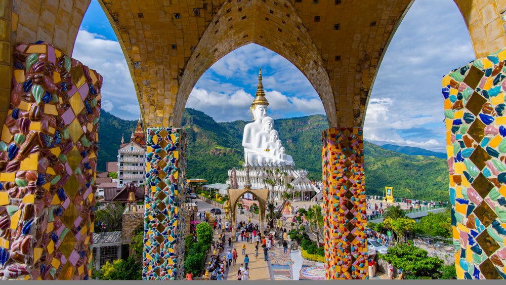 พระพุทธรูปสีขาวขนาดใหญ่ตั้งอยู่ที่วัดบนภูเขา ล้อมรอบด้วยซุ้มประตูที่ตกแต่งอย่างวิจิตรด้วยกระเบื้องโมเสกสีสันสดใส และมีผู้มาเยือนจำนวนมากอยู่ด้านล่าง — เป็นสถานที่ท่องเที่ยวเพชรบูรณ์ที่เป็นสัญลักษณ์อย่างแท้จริง ซึ่งดึงดูดนักท่องเที่ยวที่แสวงหาทั้งความงามและความสงบ.