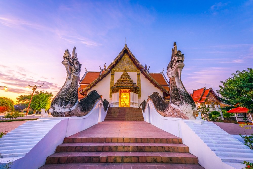 วัดไทยแบบดั้งเดิมที่มีรูปปั้นมังกรประดับอย่างวิจิตรตั้งอยู่ทั้งสองข้างของบันไดทางเข้า ท่ามกลางท้องฟ้าสีสันสดใสยามพระอาทิตย์ตกดิน — ภาพอันเป็นสัญลักษณ์นี้ถ่ายทอดเสน่ห์ของที่เที่ยวภาคเหนือได้อย่างสมบูรณ์แบบ สำหรับผู้ที่ต้องการสำรวจความมหัศจรรย์ทางวัฒนธรรมของภาคเหนือของไทย.