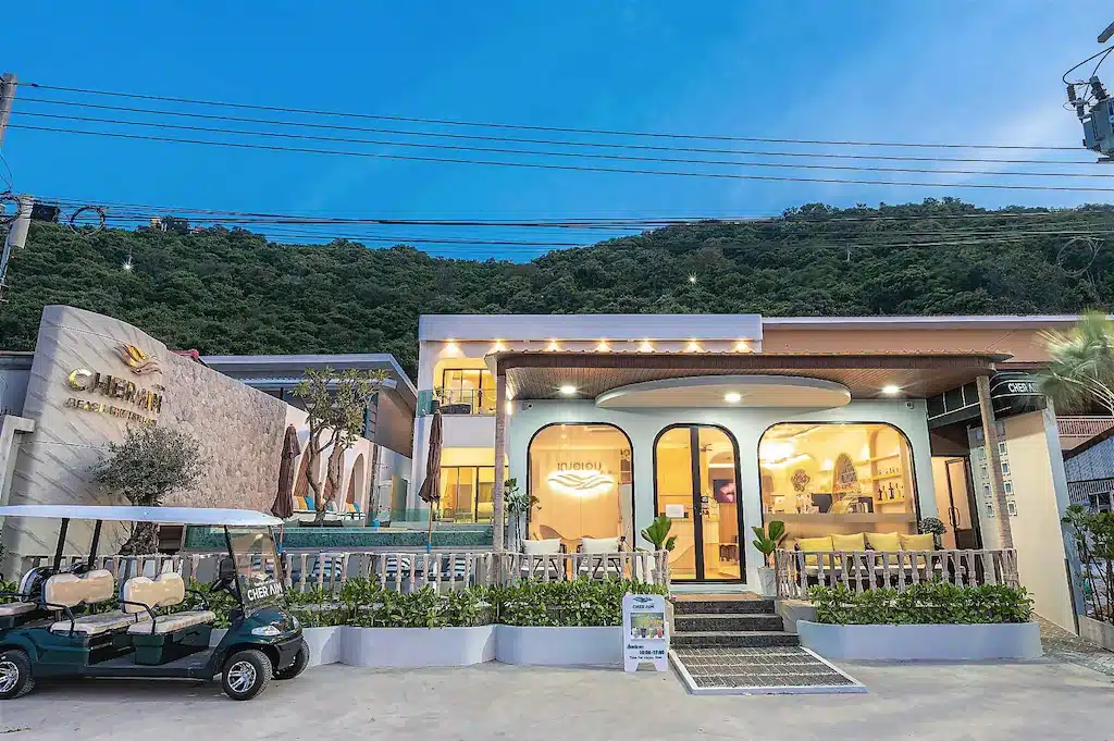 ภาพด้านนอกของ Cher Aim Cafe and Resort ซึ่งเป็นที่พักราคาประหยัดบนเกาะลัน มีรถกอล์ฟจอดอยู่ด้านหน้าและป้ายแสดงเวลาเปิด-ปิด.