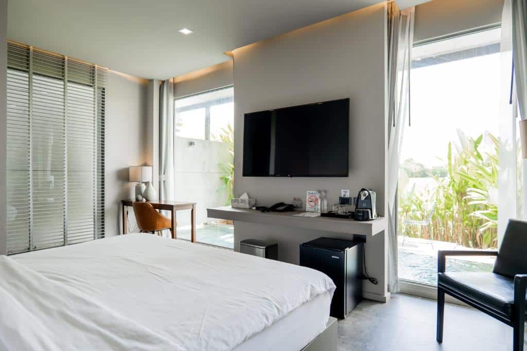 ห้องพักโรงแรมสไตล์ทันสมัยสำหรับผู้ที่ชื่นชอบการท่องเที่ยวในเชียงราย พร้อมด้วยเตียงนอน โทรทัศน์ติดผนัง โต๊ะทำงาน ตู้เย็นขนาดเล็ก และประตูแก้วที่เปิดออกสู่พื้นที่กลางแจ้งส่วนตัว.