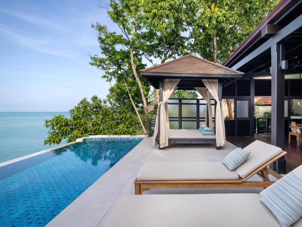 สระว่ายน้ำแบบอินฟินิตี้ที่ที่พักแห่งนี้ในเกาะสมุย มีวิวทะเลที่สวยงาม พร้อมด้วยคาบานาข้างสระและเก้าอี้พักผ่อนบนพื้นหิน.