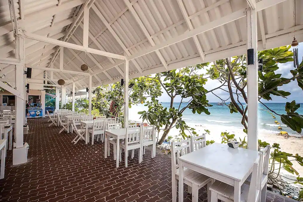 ร้านอาหารริมชายหาดแบบเปิดโล่ง พร้อมโต๊ะและเก้าอี้สีขาว ที่สามารถมองเห็นวิวทะเลได้ จากที่พักราคาประหยัดบนเกาะลันนี้.