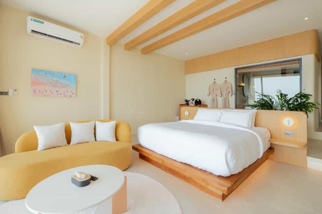 ห้องพักในโรงแรมบนเกาะลัน ที่มีเตียงแบบแพลตฟอร์ม โซฟาสีเหลืองรูปโค้ง โต๊ะกาแฟรูปวงกลม และเครื่องปรับอากาศติดผนัง.