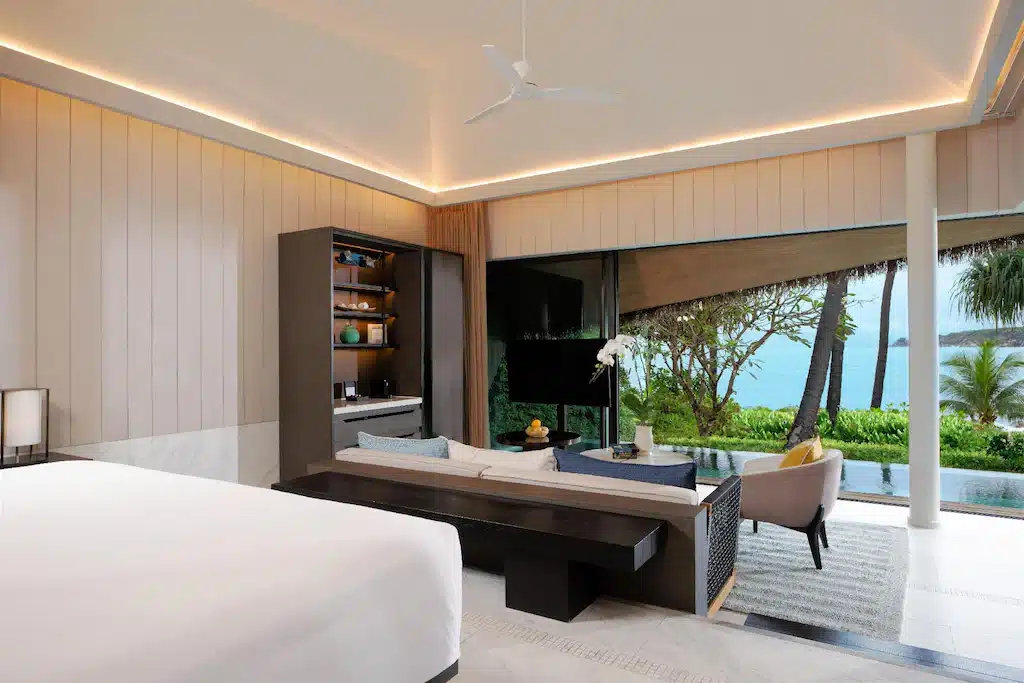 ห้องพักในโรงแรมที่มีเตียง โซฟาหันหน้าสู่โทรทัศน์ และประตูแก้วเลื่อนที่เปิดออกสู่สระว่ายน้ำส่วนตัว ซึ่งสามารถมองเห็นทะเลได้ที่ที่พักเกาะสมุยแห่งนี้.
