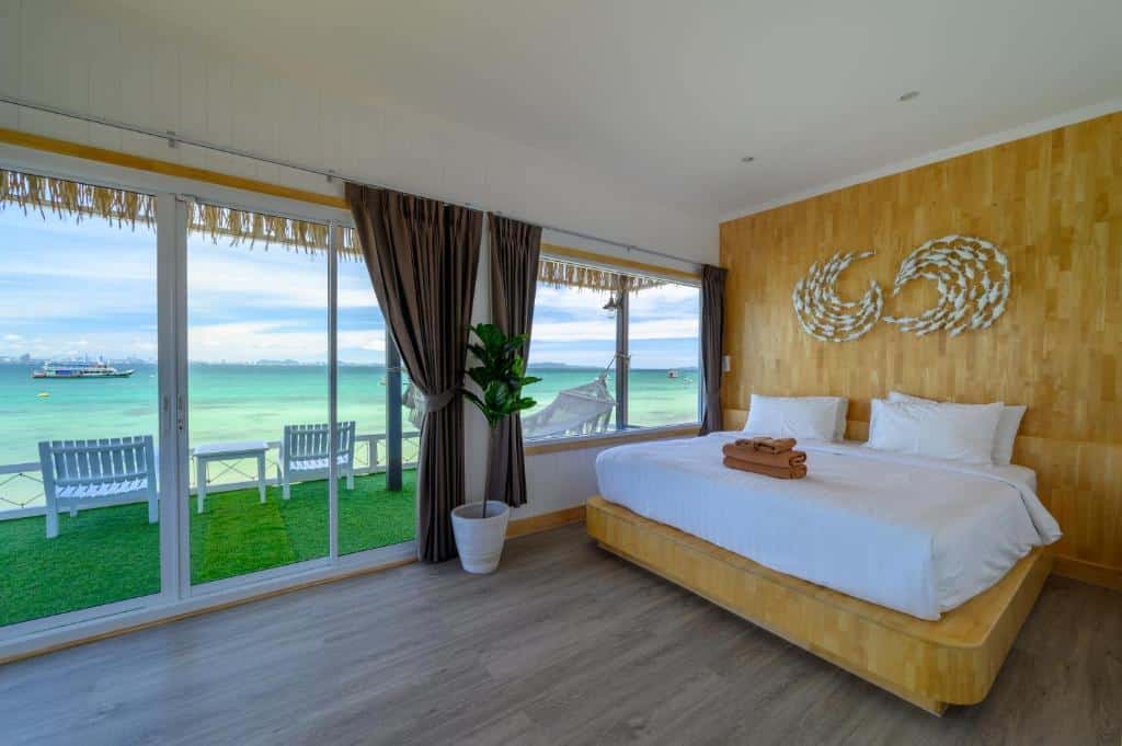 ห้องพักในโรงแรมบนเกาะลาร์น ที่มีเตียงควีน ผนังบุไม้ และประตูเลื่อนกระจกที่เปิดออกสู่ระเบียงซึ่งมองเห็นทะเล.