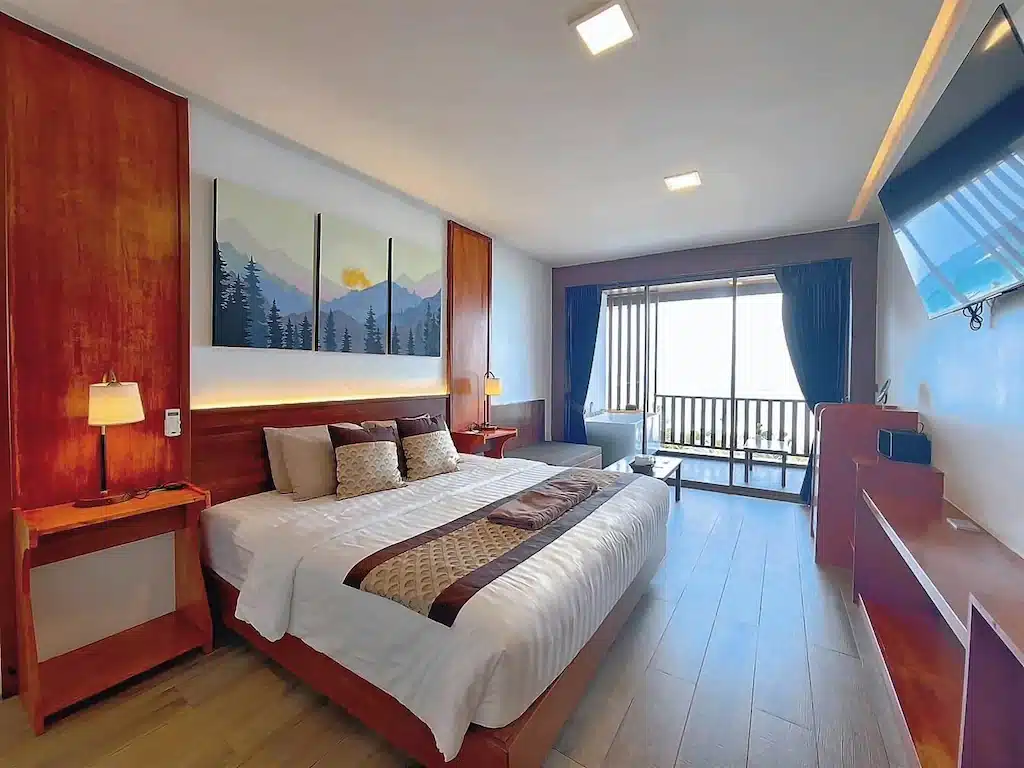 ห้องพักในโรงแรมที่มีเตียงคิงไซส์ ตกแต่งด้วยไม้ และมีระเบียงส่วนตัวที่มองออกไปสู่พื้นที่กลางแจ้งที่สว่างสดใส เป็นที่พักบนเกาะล้านที่สมบูรณ์แบบสำหรับคุณ.