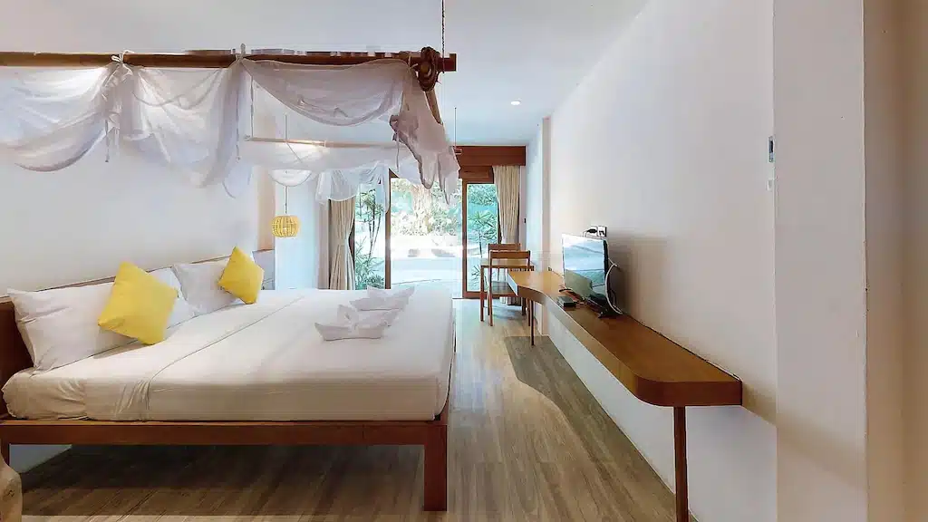 ห้องพักในโรงแรมบนเกาะลาร์น ที่มีเตียงมีม่านคลุม โต๊ะทำงานยาวติดผนัง และโทรทัศน์ ซึ่งเปิดออกสู่ลานระเบียง.