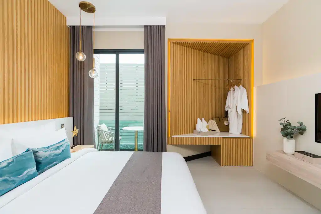 ห้องพักในโรงแรมแห่งนี้มีเตียงนอน ระเบียงเล็กพร้อมที่นั่งกลางแจ้ง และพื้นที่ตู้เสื้อผ้าแบบฝังผนังที่มีชุดคลุมอาบน้ำแขวนไว้ ที่พักราคาประหยัดบนเกาะลันแห่งนี้.