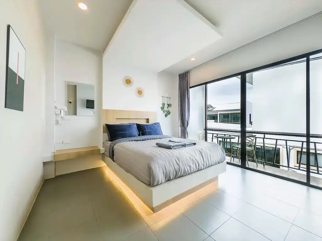 ห้องนอนในโรงแรมที่มีเตียงควีนไซส์ โต๊ะข้างเตียงแบบลอยตัว และระเบียงพร้อมที่นั่งกลางแจ้ง ที่ที่พักเกาะล้านติดทะเลแห่งนี้.