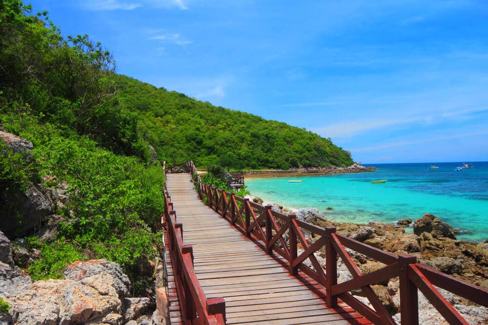 ทางเดินไม้โค้งไปตามชายฝั่งหิน นำสู่ชายหาดที่มีน้ำสีเทอร์ควอยซ์และเนินเขาสีเขียว ซึ่งเหมาะอย่างยิ่งสำหรับแขกที่กำลังมองหาที่พักราคาประหยัดบนเกาะลัน.
