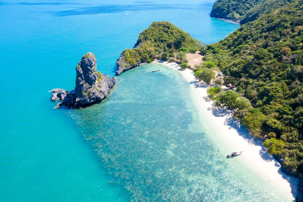 ภาพจากอากาศของอ่าวหาดทรายขาวใน ที่เที่ยวเกาะสมุย 2026 ซึ่งมีหินขนาดใหญ่ตั้งตระหง่านในน้ำสีเทอร์ควอยซ์ และป่าเขียวชอุ่มหนาแน่นตามแนวชายฝั่ง.