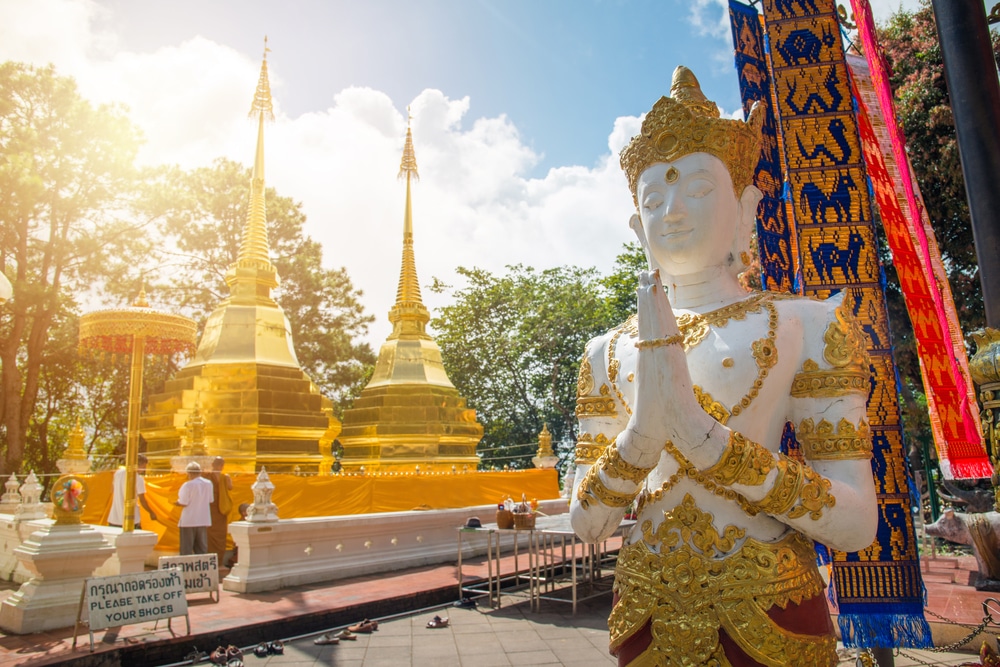 รูปปั้นสีขาวของเทพเจ้าในท่าสวดมนต์ตั้งอยู่หน้าเจดีย์ทองสององค์ ณ วัดพุทธ ซึ่งเป็นจุดท่องเที่ยวยอดนิยมสำหรับผู้ที่เที่ยวเชียงราย.