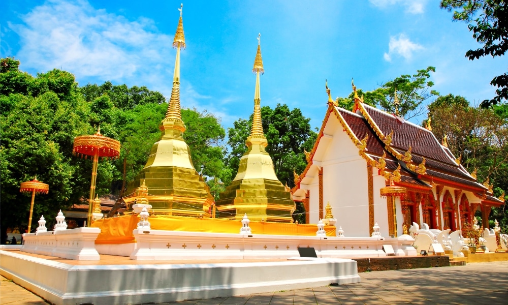 เจดีย์ทองสององค์และวัดพุทธสีขาวที่ตกแต่งอย่างวิจิตร ตั้งอยู่ท่ามกลางท้องฟ้าสีฟ้าและต้นไม้สีเขียว ณ สถานที่ท่องเที่ยวยอดนิยมในเชียงราย.